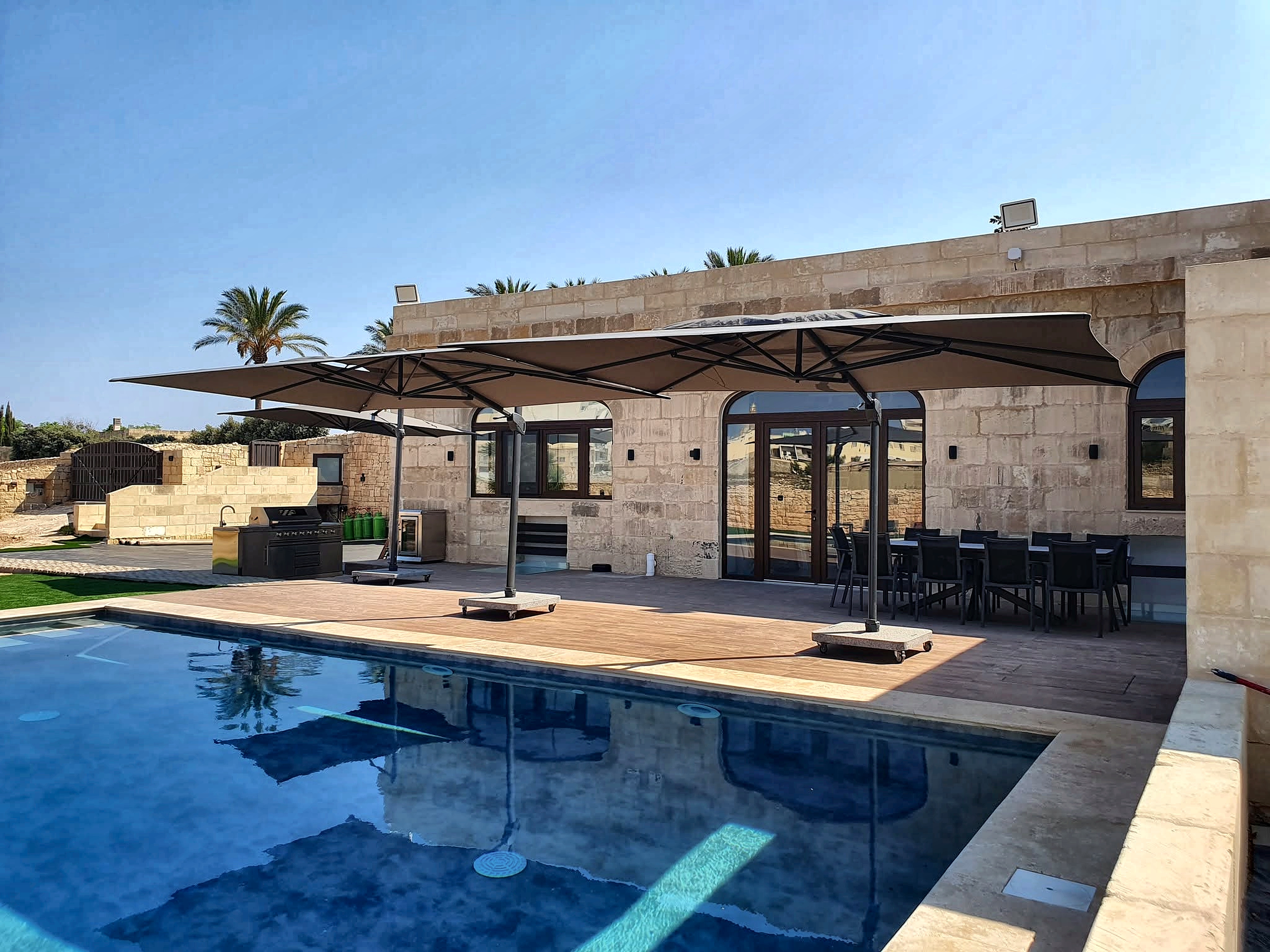 Expansive poolside terrace with modern sunshades and farmhouse stone facade
